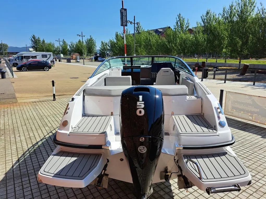 A motorboat with a visible engine labelled "150", parked at a quay with trees and vehicles in the background.